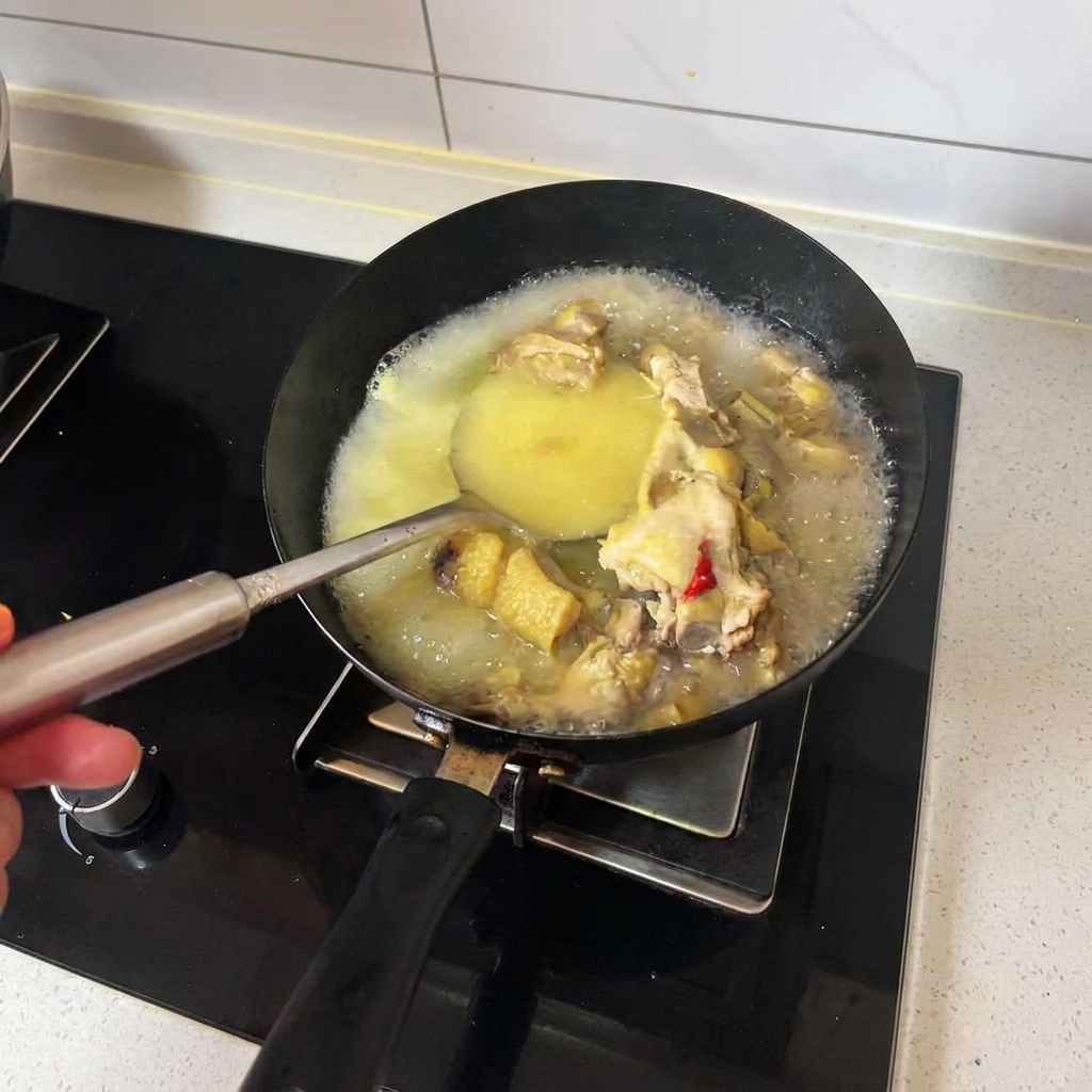 Un mestolo che mescola brodo di pollo caldo dorato e pezzi di pollo cotto in un wok nero.