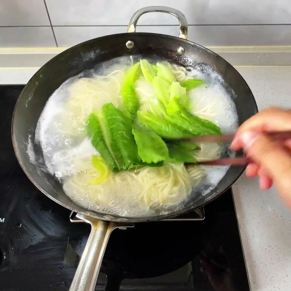 Noodle sottili e verdure fresche a foglia bollenti in un wok dacqua frizzante, mescolati con bacchette di legno.