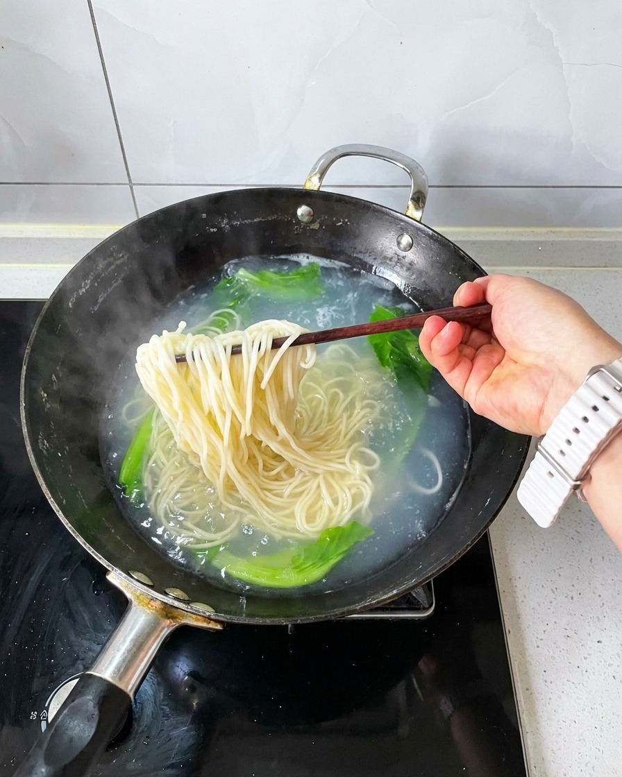 Bacchette di legno che sollevano un mucchio di noodle cotti e verdure sbollentate fuori dallacqua bollente.
