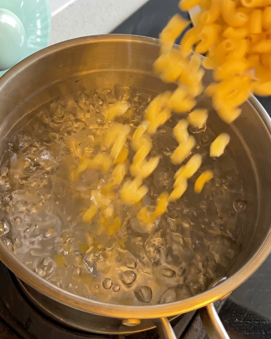 Pasta corta versata in una pentola di acqua bollente.