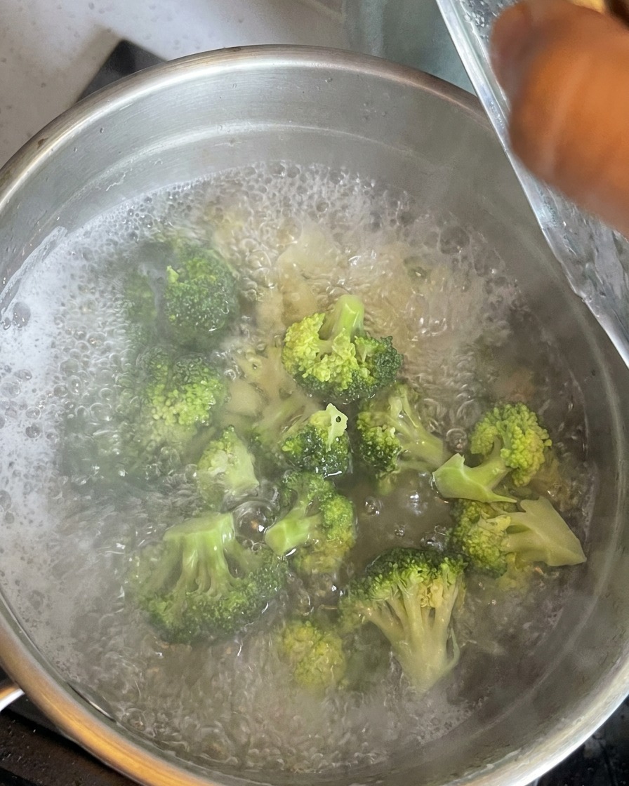 Cimette di broccoli verdi immerse in acqua bollente con i maccheroni.