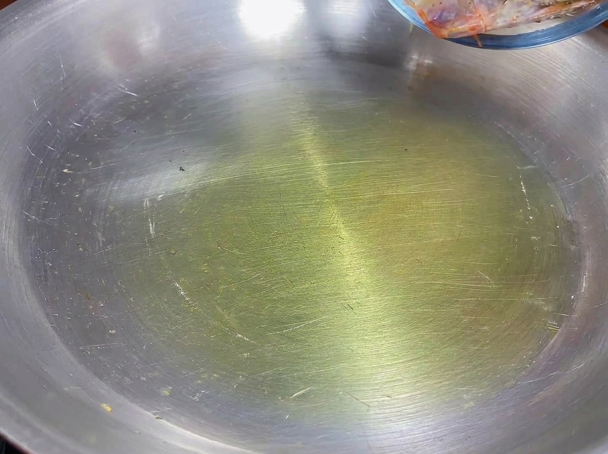 Teste di gambero che soffriggono in olio doliva in una padella di acciaio inox.