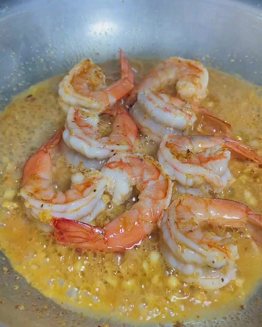 Panna versata in una padella contenente i gamberi cotti e laglio.