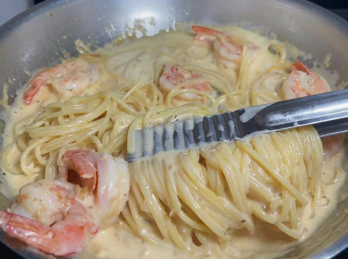 La pasta e i gamberi vengono saltati in padella per amalgamarsi con la salsa cremosa.