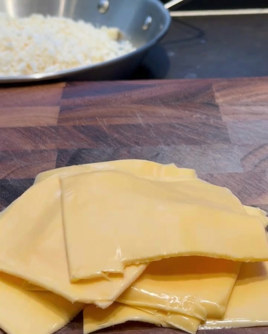 Fette di formaggio cheddar tagliate in piccoli pezzi su un tagliere di legno.