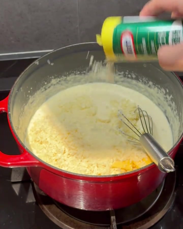 Formaggio in polvere aggiunto e mescolato con una frusta in una crema dentro una pentola rossa.