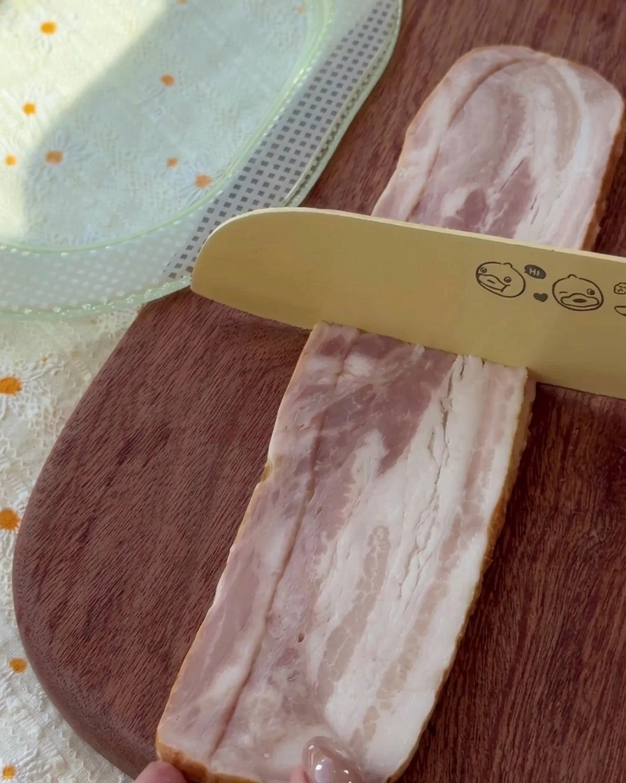 Strisce di bacon crudo tagliate a pezzetti uniformi su un tagliere in legno.