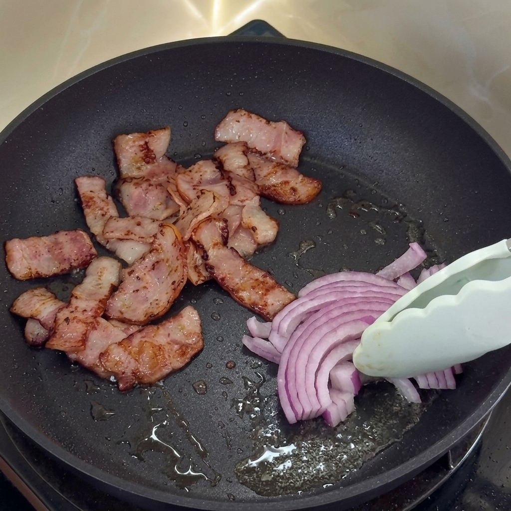 Cipolle rosse che cuociono nel grasso di cottura del bacon insieme ai pezzetti di bacon croccante.