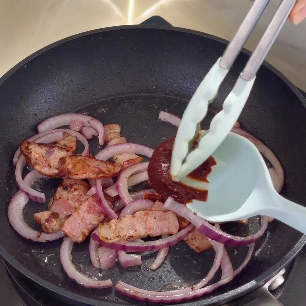 La salsa piccante coreana viene mescolata al bacon e alle cipolle in padella.