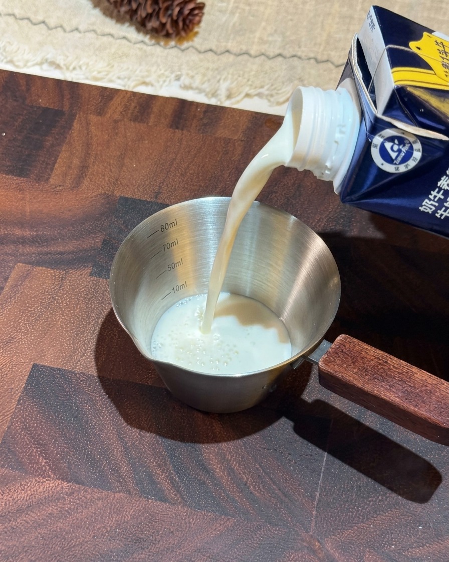 Del latte bianco viene versato da un cartone blu in un piccolo misurino di acciaio inossidabile con manico in legno.