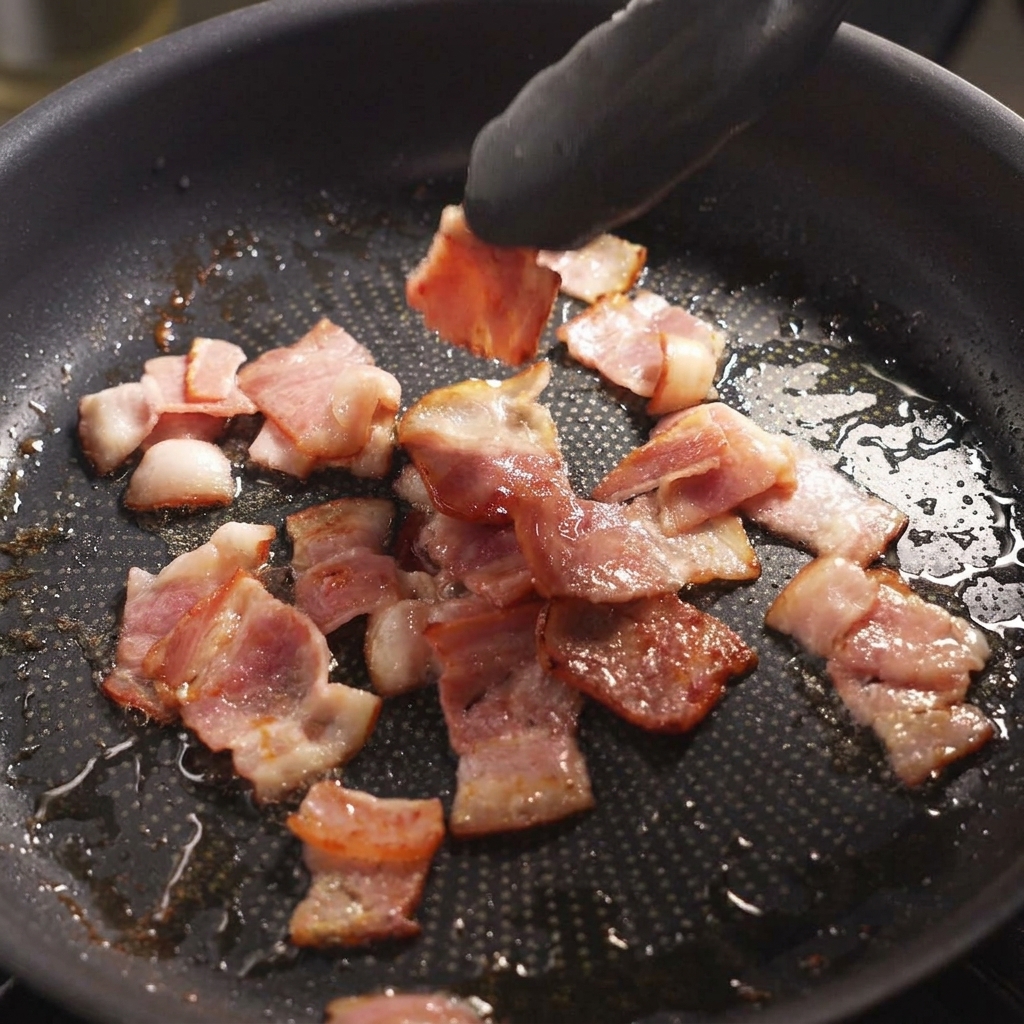 Pinze nere che girano pezzi di pancetta sfrigolante in una padella.