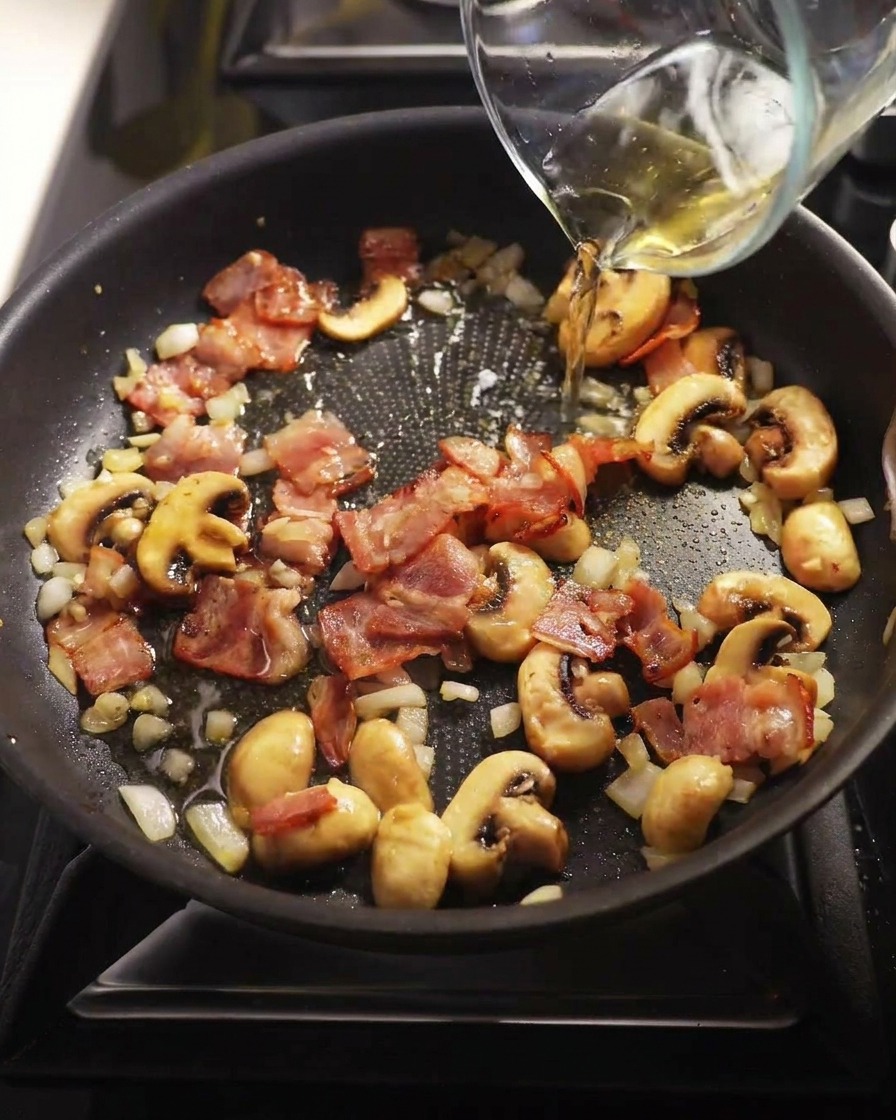Vino bianco versato in padella sui funghi e la pancetta.