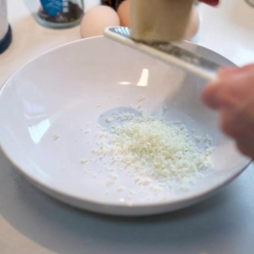 Grattugiare parmigiano fresco in una ciotola bianca pulita.