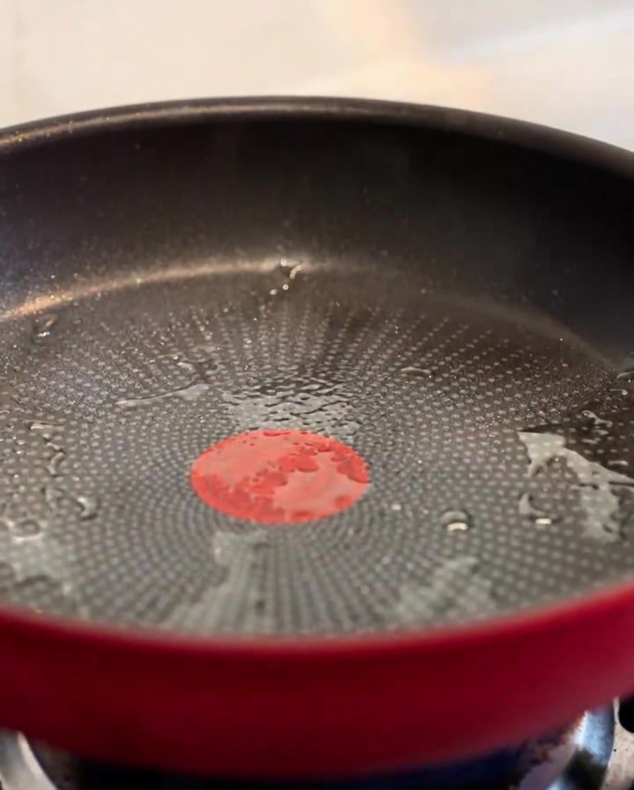 Pezzetti di pancetta croccante che sfrigolano in una padella rossa.