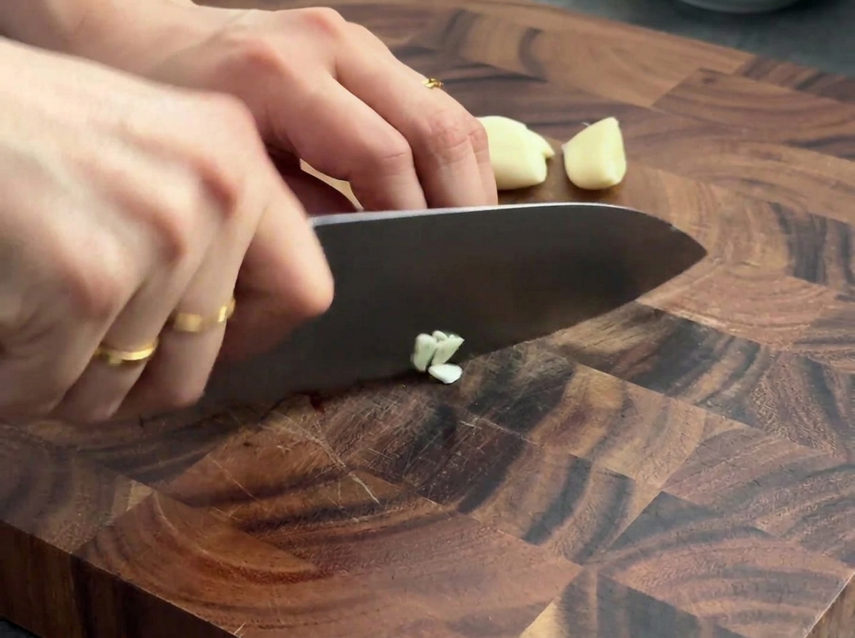 Spicchi daglio tritati su un tagliere di legno con un coltello da chef.