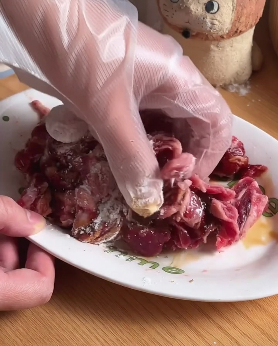Strisce di manzo mescolate con condimenti e ingredienti della marinata in una ciotola bianca.