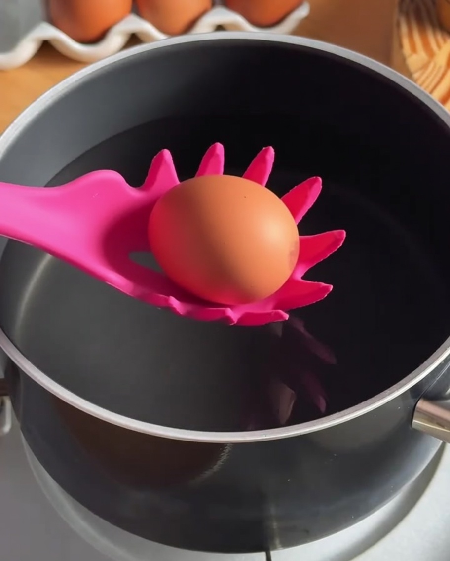 Un uovo immerso in una pentola di acqua calda usando un cucchiaio forato in silicone.