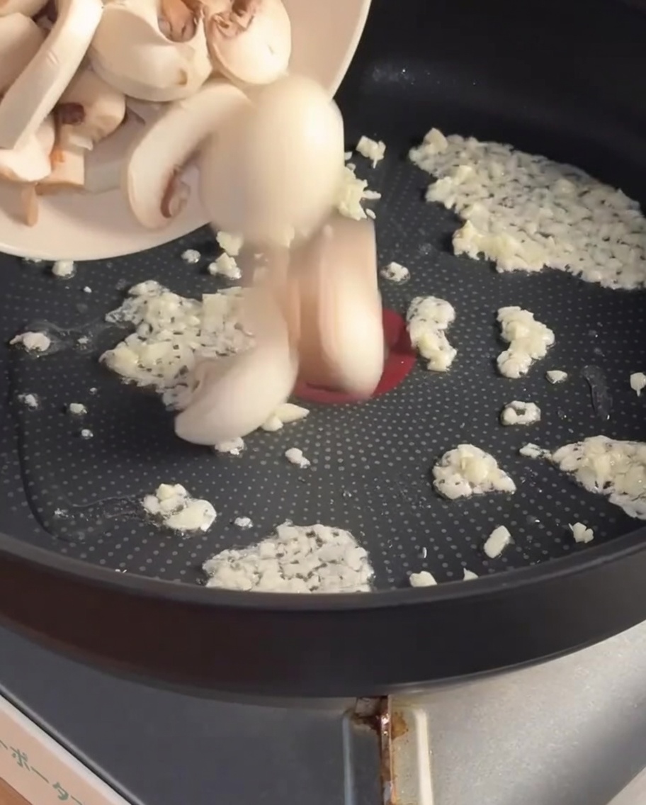 Funghi affettati aggiunti alla padella con laglio rosolato.
