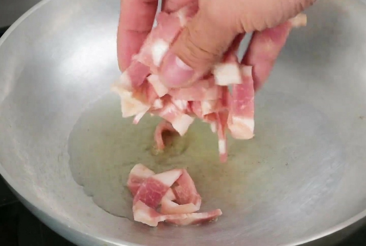 Strisce di pancetta che friggono in padella con olio doliva sfrigolante.