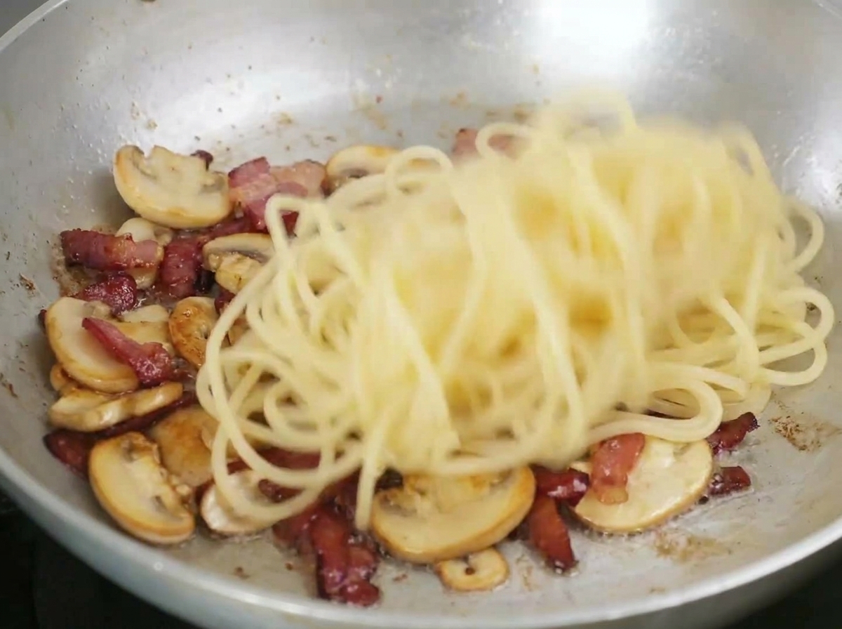 Spaghetti saltati in padella con pancetta rosolata e funghi a fette.