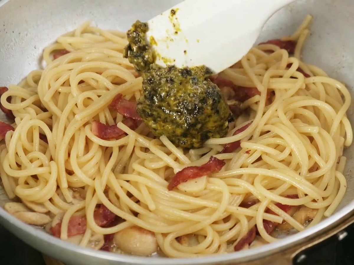 Una spatola che mescola la scura e aromatica salsa al tartufo nero in una padella di pasta, aglio e pancetta.