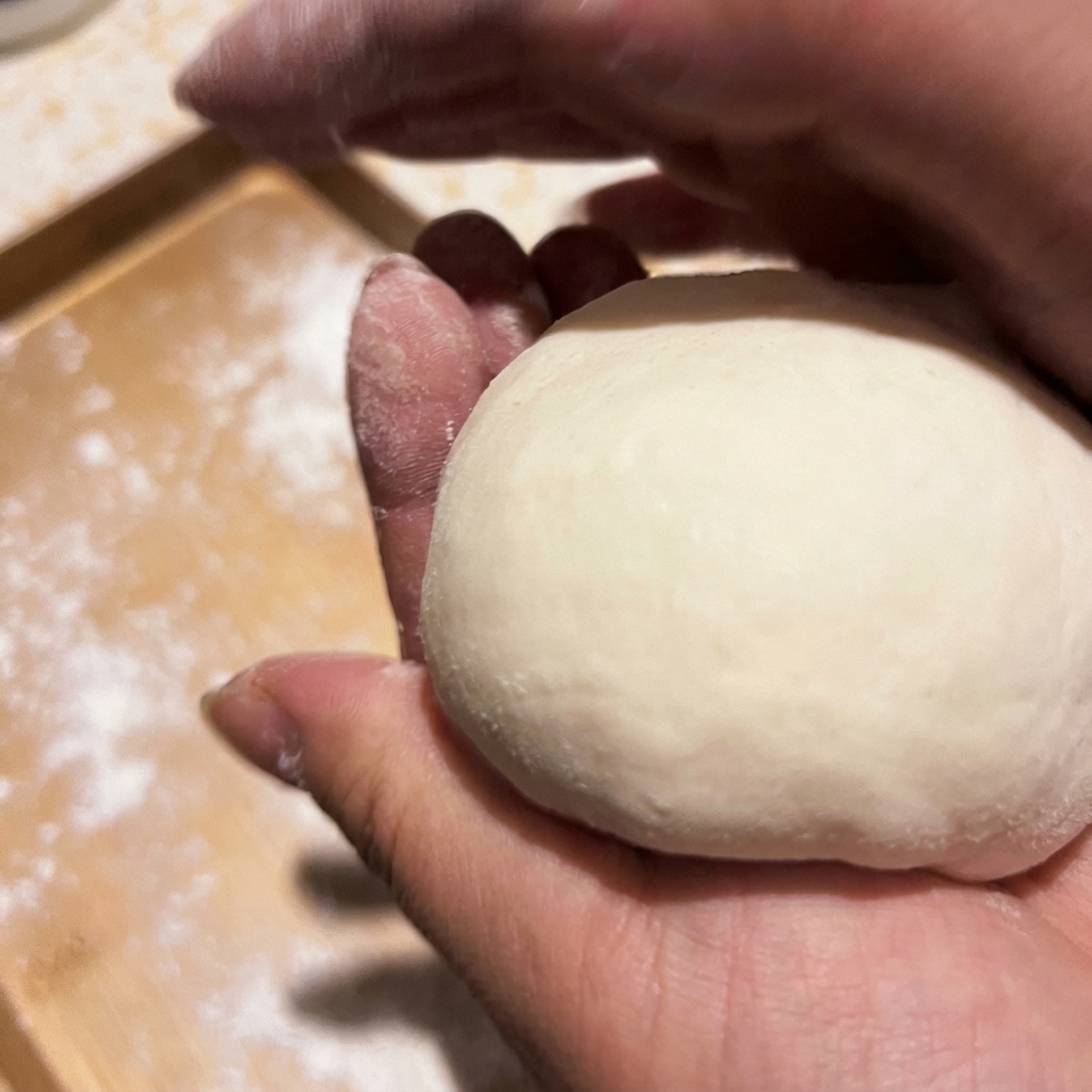 Mani che modellano una porzione di impasto crudo in una pallina liscia.