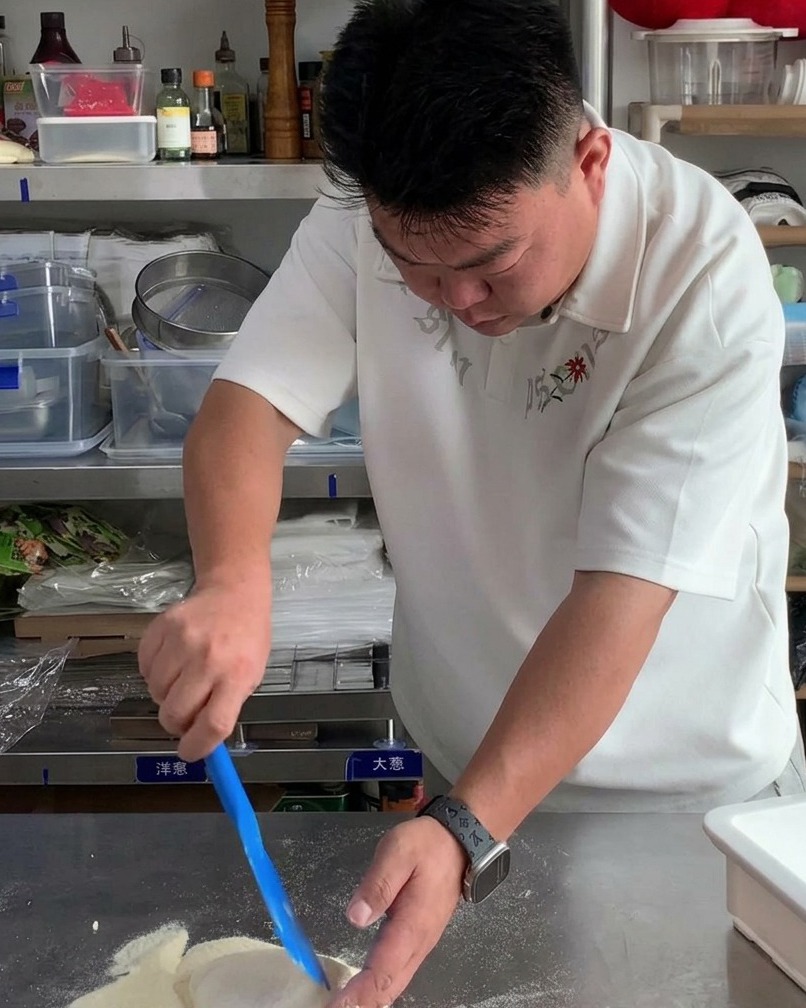 Una porzione di impasto crudo per pizza sollevata da un contenitore bianco con un raschietto blu.