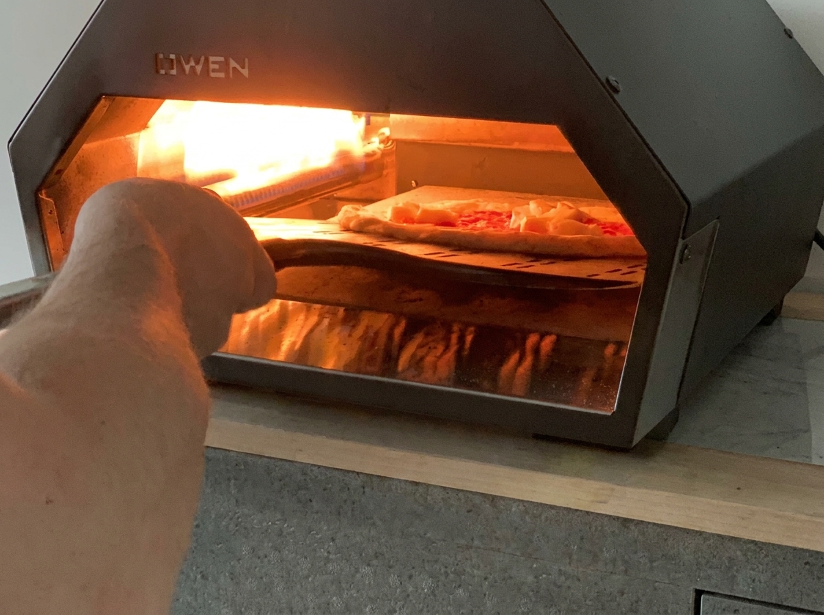 Una pala da pizza che introduce una pizza Margherita cruda in un forno a gas da tavolo.