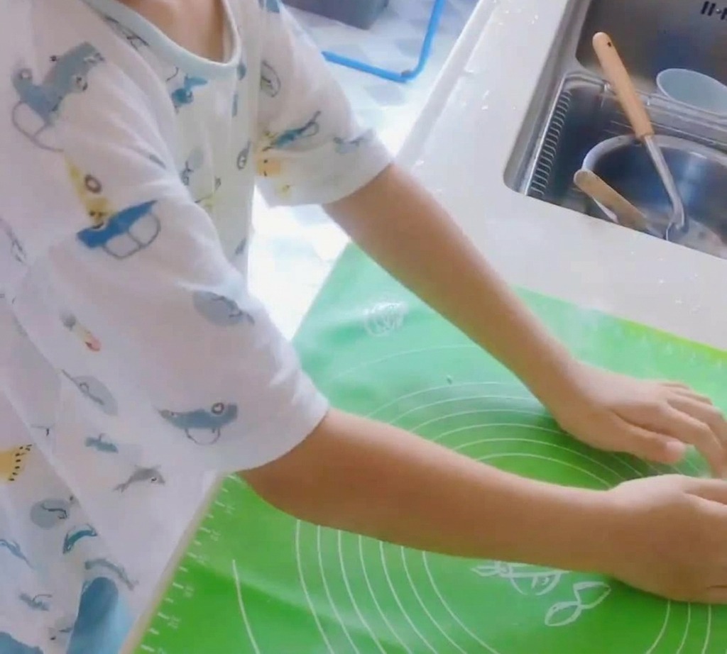 Un panetto di impasto per pizza lavorato su un tappetino in silicone verde.