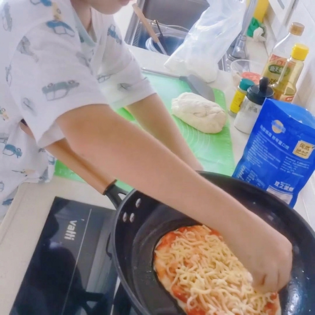 Primo piano di una base per pizza in padella coperta da uno strato di mozzarella grattugiata.