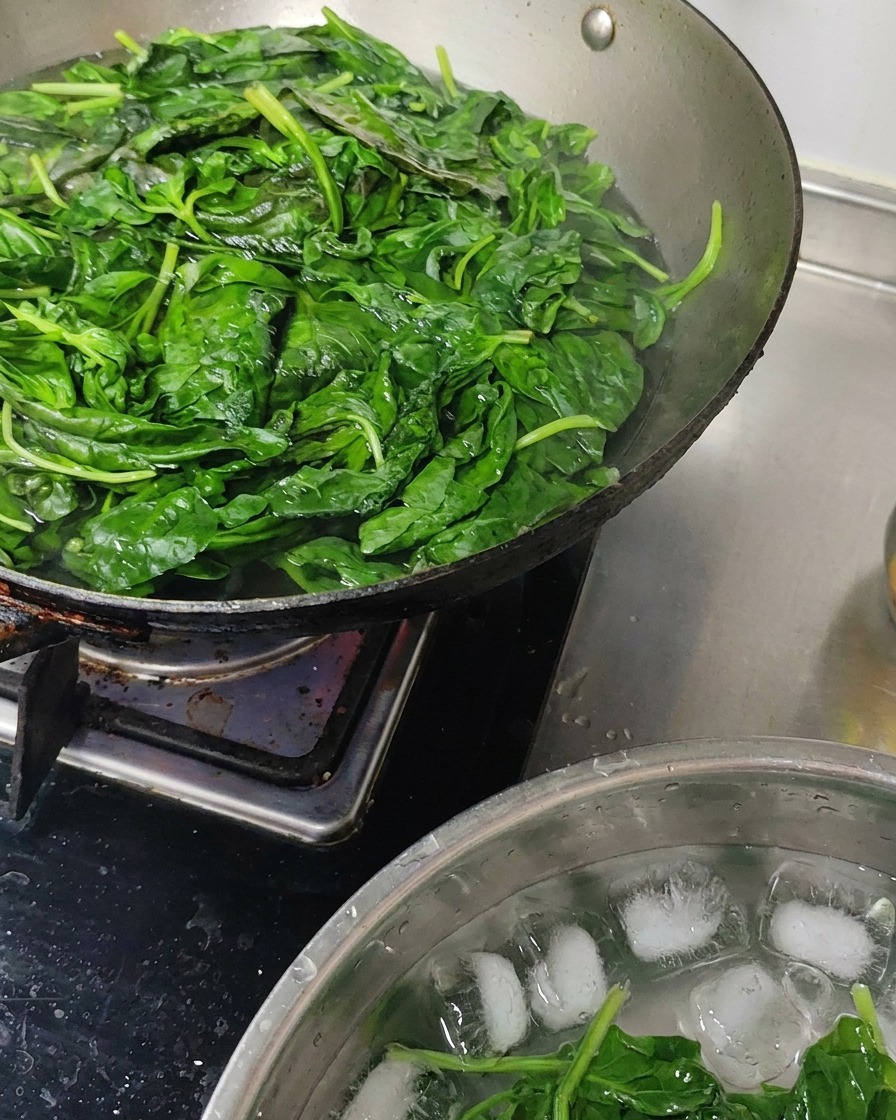 Foglie di basilico sbollentate raffreddate in una ciotola piena di acqua e ghiaccio.
