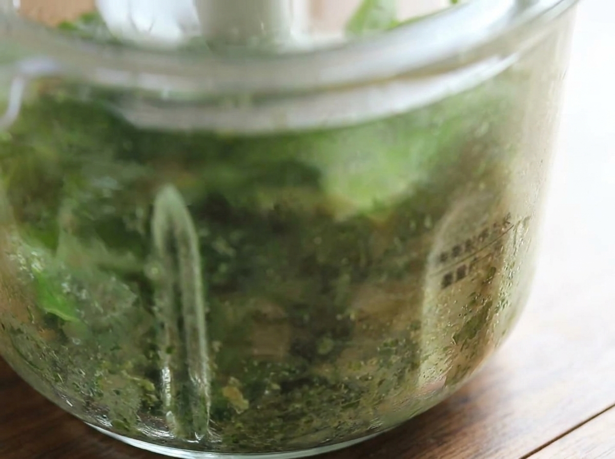 Primo piano del robot da cucina che mostra il pesto al basilico appena frullato di colore verde brillante.