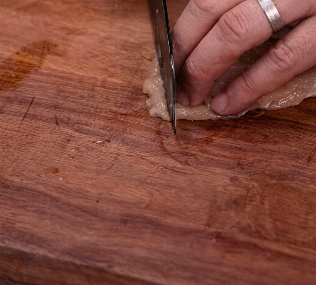 Petto di pollo crudo tagliato a listarelle uniformi su un tagliere di legno.