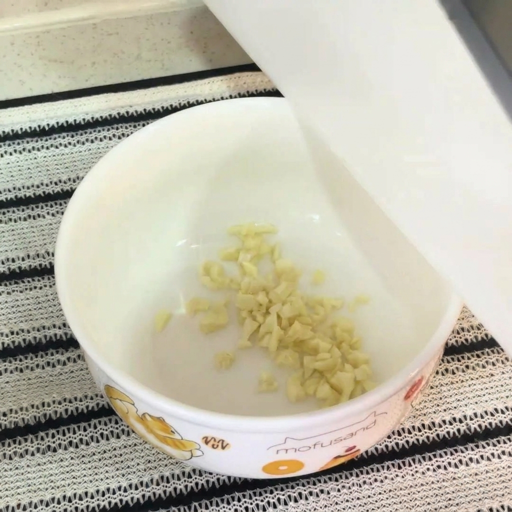Primo piano di una ciotola bianca contenente aglio tritato, tuorlo duovo crudo, condimento per noodles istantanei e maionese, pronta per essere mescolata in una base per zuppa.