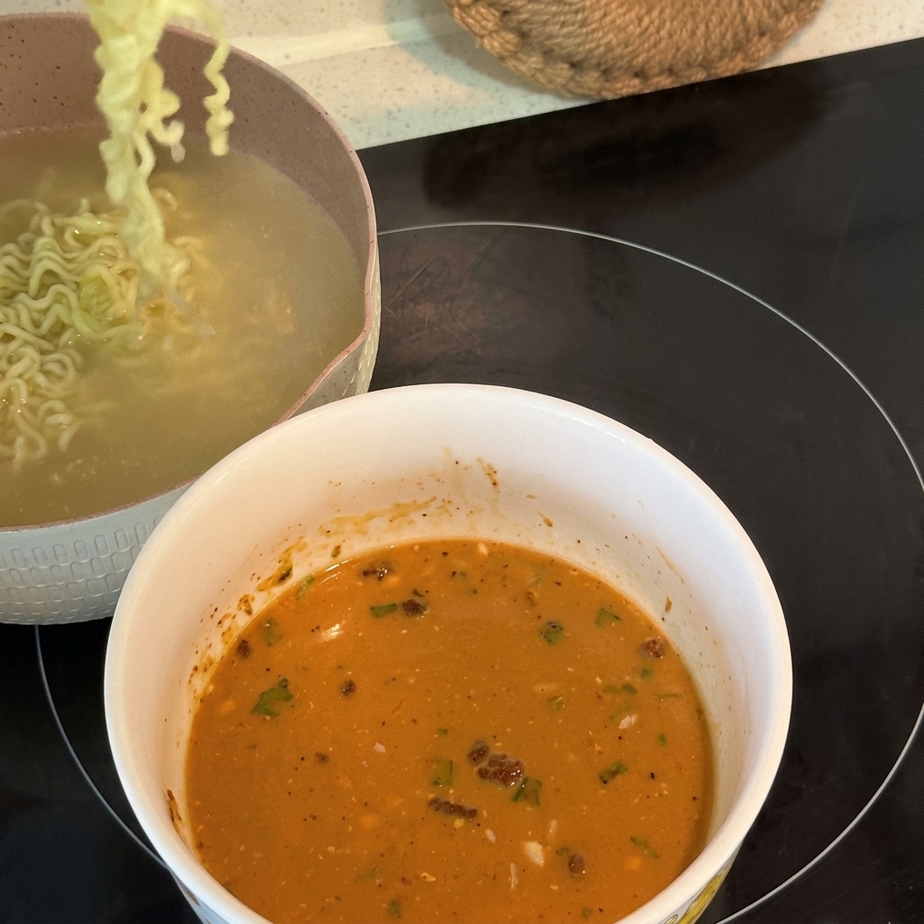 Noodles ramen ricci cotti sollevati e trasferiti in una ciotola riempita con una base di zuppa cremosa ed emulsionata.