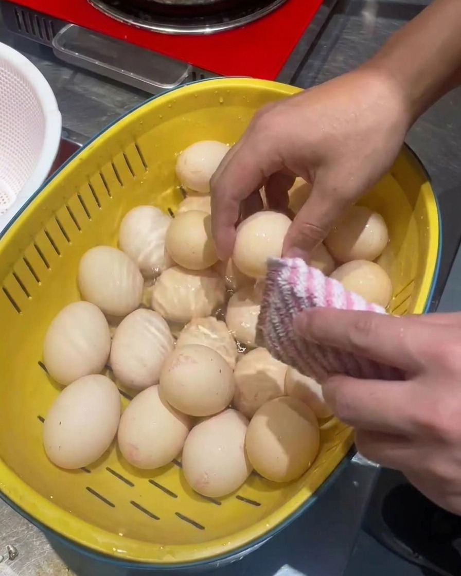 Uova pulite in uno scolapasta giallo con una spugnetta abrasiva.