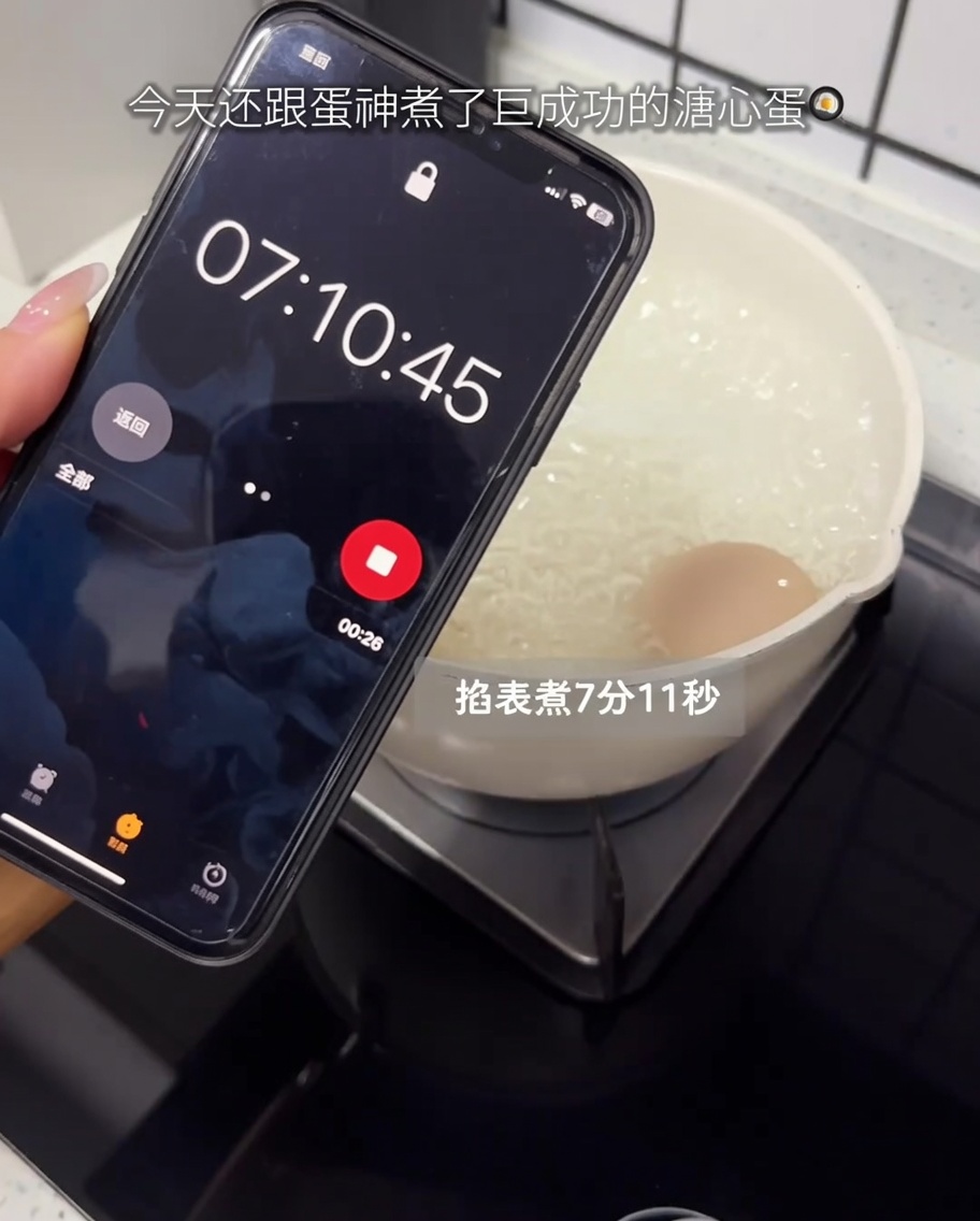 Un uovo crudo che bolle in una pentola sul fornello con un timer sul cellulare in primo piano.