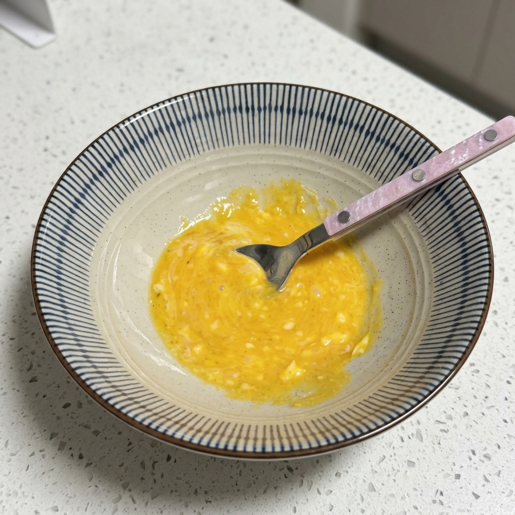Una ciotola contenente una base di brodo gialla e cremosa che viene mescolata con un cucchiaio.