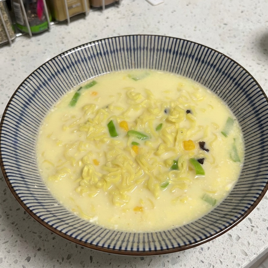 Un primo piano di fettine di manzo aggiunte a una ciotola di noodles e brodo cremoso.