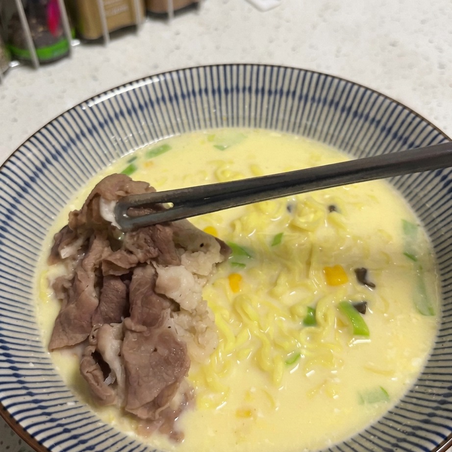 Un cucchiaio di chicchi di mais dorati cosparsi sopra una ciotola di ramen.