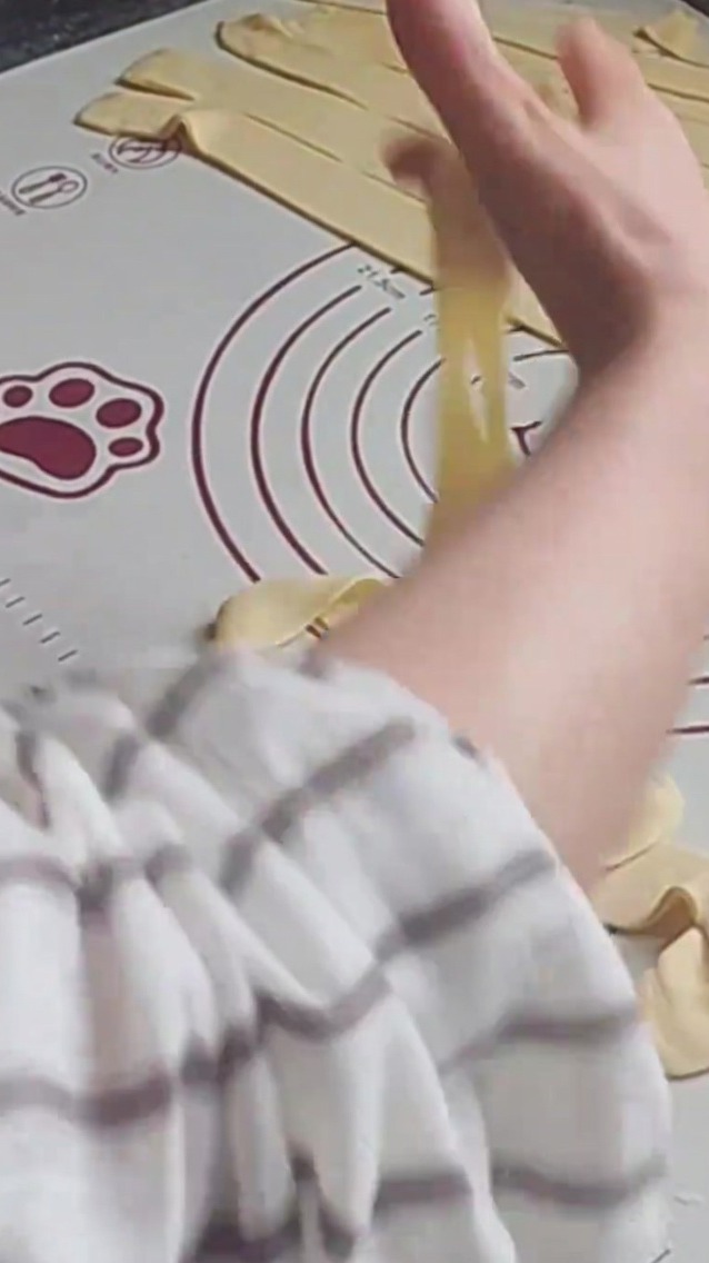 Mani che allungano un filo di impasto su un tappetino in silicone, preparandolo per la cottura.