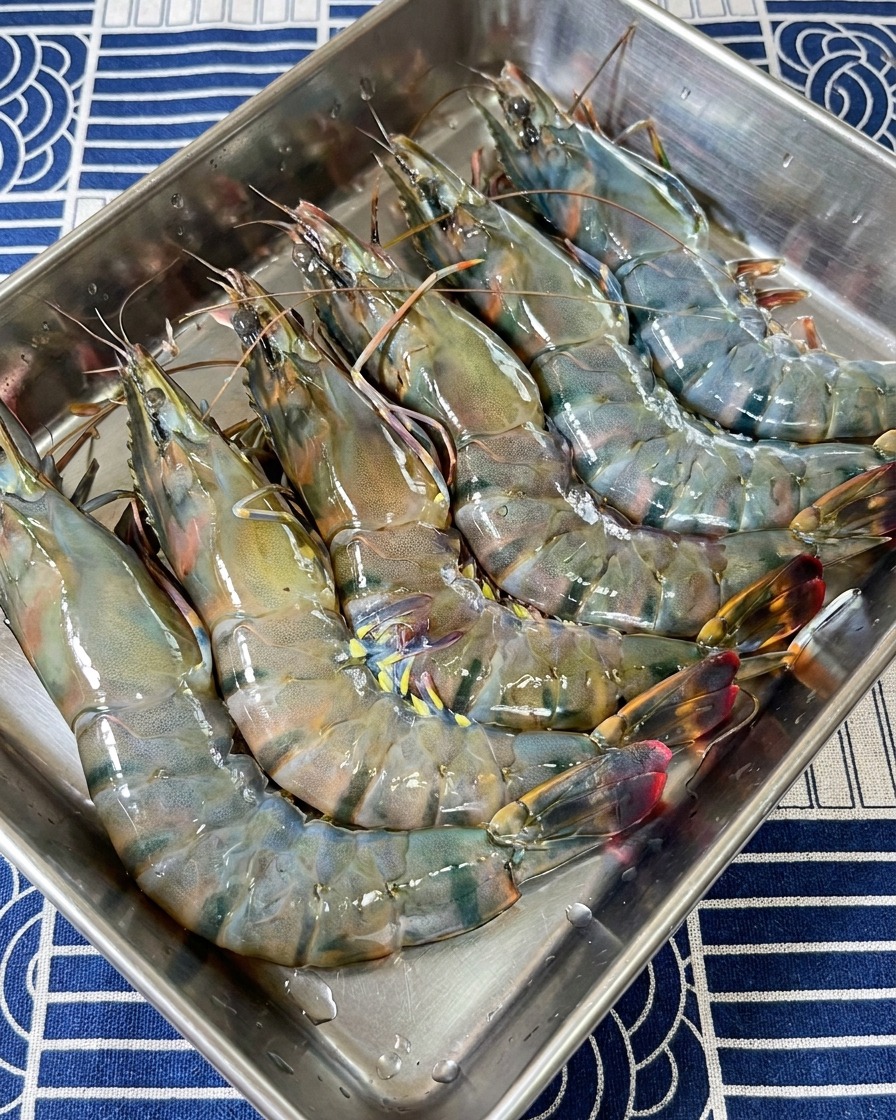 Una selezione di teste e carapaci crudi di gambero tigre nero disposti in un vassoio di preparazione in acciaio inossidabile.