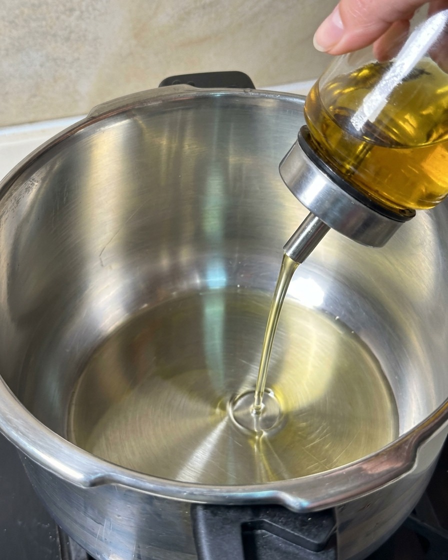 Olio per friggere versato da un dosatore in vetro in una pentola di acciaio inossidabile pulita.
