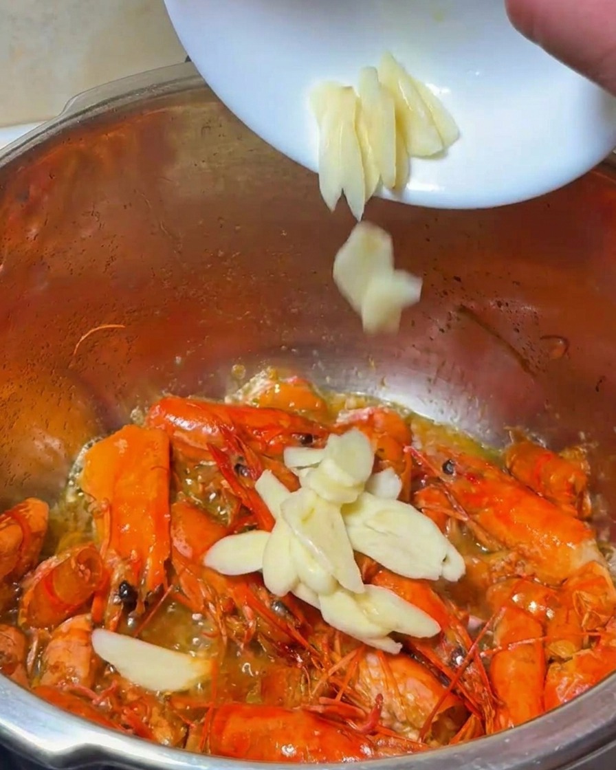 Aglio e cipolla a fette aggiunti alla pentola dei carapaci di gambero in frittura.