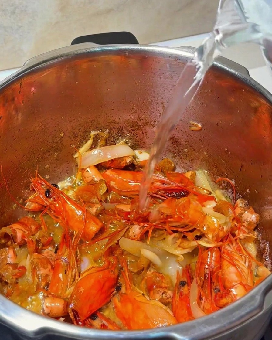 Acqua versata da una brocca di vetro in una pentola contenente carapaci di gamberi e aromi.