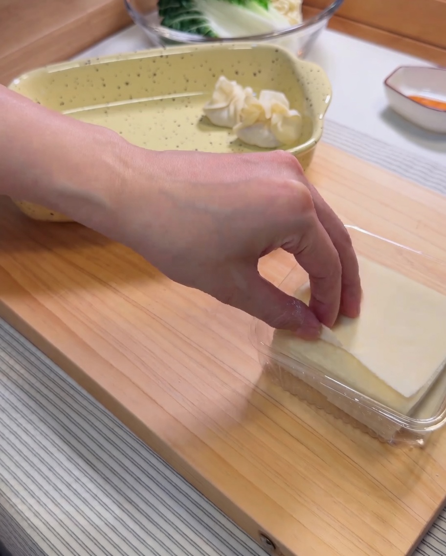 Un impasto per wonton sul palmo di una mano con il ripieno di gamberi aggiunto al centro usando una sac à poche.