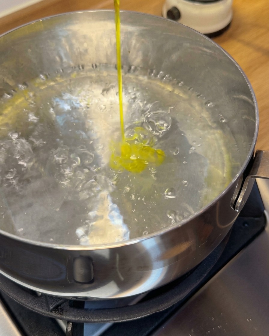 I wonton di gamberi crudi vengono immersi in una pentola di acqua bollente usando una schiumarola.