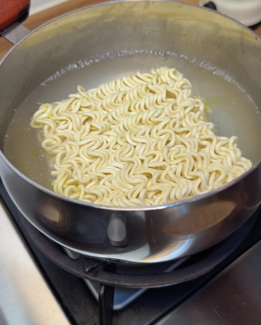 Un blocco di noodles istantanei immerso nellacqua bollente, in cottura.