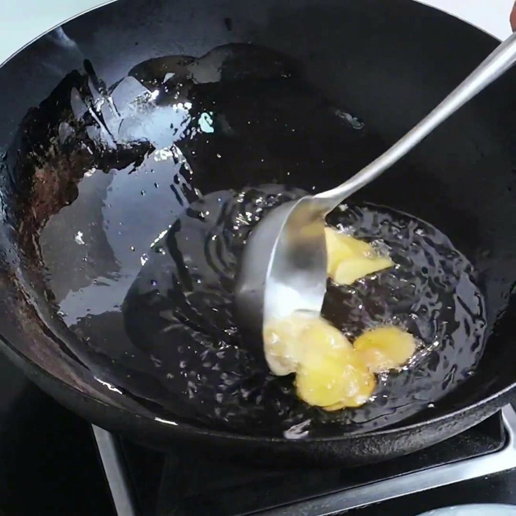 Fette di zenzero e teste di gambero che sfrigolano in un wok con olio caldo.