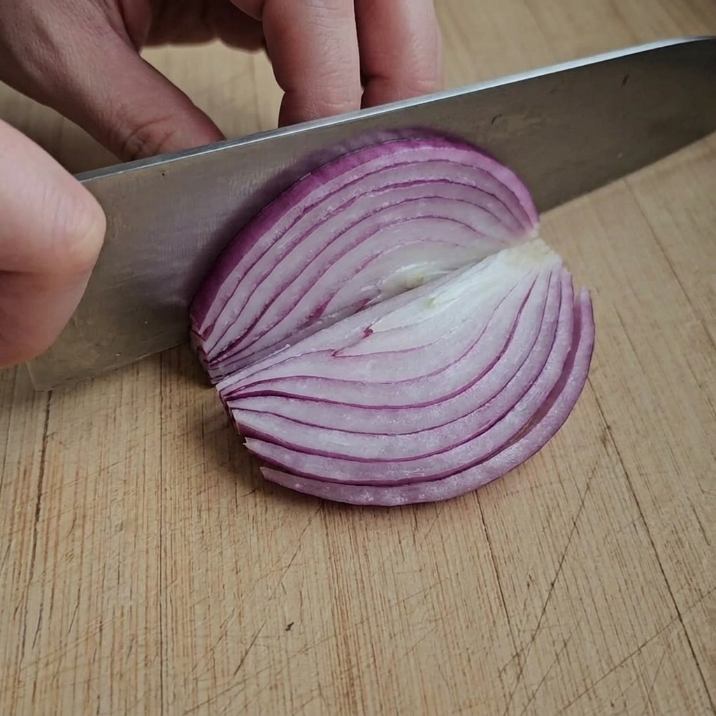 Fette sottili di cipolla rossa disposte su un tagliere di legno.